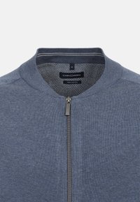 Cardigan zippé en coton bleu foncé avec un col et des poignets côtelés. Présente une texture subtile et un petit logo sur le côté gauche.