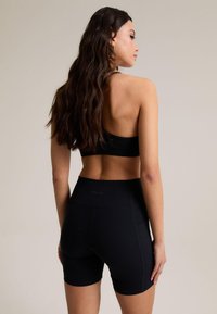 Černý sportovní outfit obsahující přiléhavou sportovní podprsenku a šortky s vysokým pasem, které ukazují hladkou látku a minimální švy s elegantním designem.