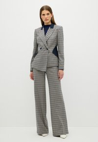 Kostkovaný oblek s dvouřadým sakem v námořnické modré barvě a širokými kalhotami. Tkanina má texturovaný, tkaný vzhled.