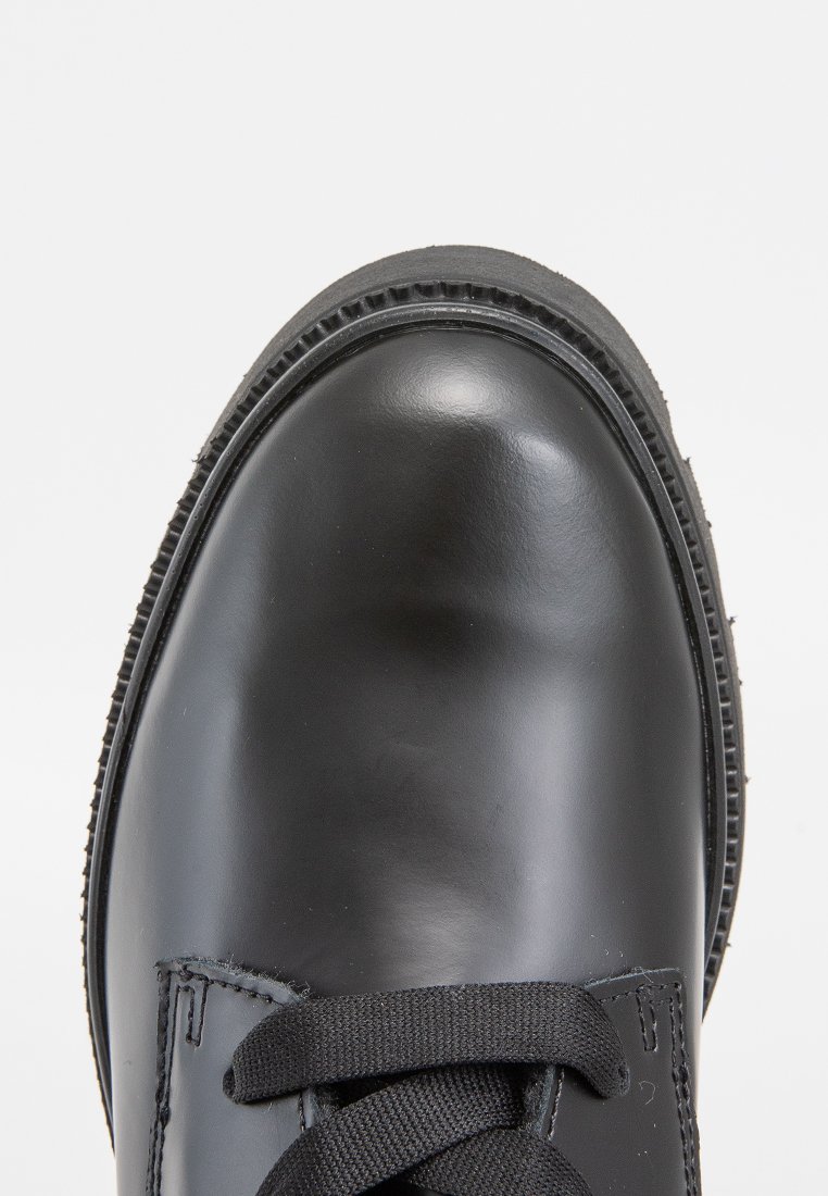 Schwarzer Lederschuh mit runder Zehenform und strukturiertem Obermaterial. Verfügt über schwarze Schnürsenkel und eine Gummisohle mit einem leichten Rillenprofil für besseren Halt.