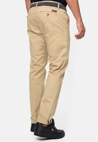 Chinos color caqui con corte recto, fabricados en algodón. Cuentan con un bolsillo trasero abotonado y un detalle de cinturón tejido. Combinados con zapatillas negras.