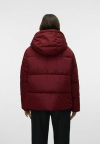 Burgunderfarget pufferjakke med stor hette, quiltet design og avslappet fasong. Teksturen ser glatt ut, med synlige sømmer og en noe cropped lengde.