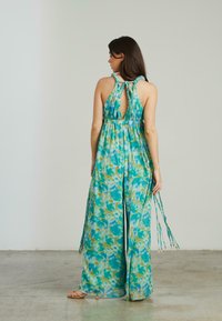 Jumpsuit fluide sans manches en tie-dye turquoise et vert. Caractéristiques : dos ouvert, taille avec cordon de serrage et longues bretelles tressées.