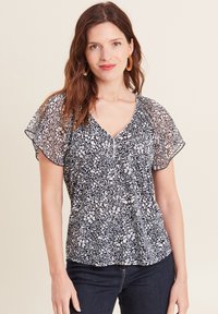 Navy blauwe blouse met een wit bloemenpatroon, korte mouwen van doorschijnend materiaal, V-hals en knoopdetails aan de voorkant.