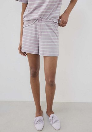 Osoba koja nosi svijetloplave i bijele prugaste kratke hlače s vezicom i odgovarajućom majicom, uparenu s bijelim tkanim obućama koje se obuvaju bez vezica.