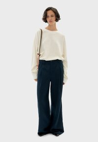 Maglietta crema a maniche lunghe, vestibilità rilassata. Pantaloni navy a vita alta a gamba larga con pinces frontali. Tiene una borsa rosa chiaro. Scarpe nere flat.
