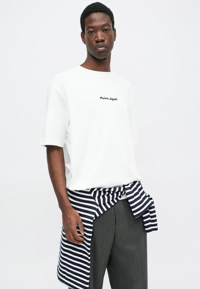White cotton t-shirt with short sleeves and black embroidered “Maison Margiela” logo. Navy and white striped fabric tied at the waist.