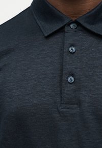 Κοντινό πλάνο σκούρου γκρι πόλο πουκάμισου με τρία σκοτεινά κουμπιά και διπλωμένο γιακά σε ένα άτομο.