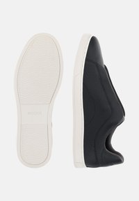 Chaussures noires en cuir à enfiler avec une surface texturée et une semelle en caoutchouc blanche. Présente une pointe arrondie et un design découpé sur les côtés.
