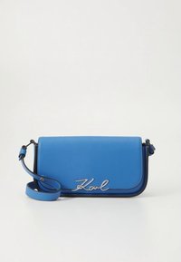 Kék bőrből készült keresztpántos táska, sima textúrával, ezüst "Karl" logóval és állítható pánttal. Téglalap alakú, lekerekített szélekkel.