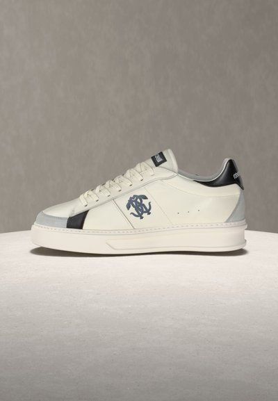 Λευκό δερμάτινο αθλητικό παπούτσι με μαύρες λεπτομέρειες, λογότυπο στο πλάι, λευκά κορδόνια και παχιά σόλα, παρουσιάζεται σε ουδέτερη επιφάνεια.