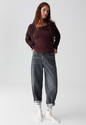 Burgundy tank top, dark brown textured cardigan, and gray tapered jeans. White socks with black design, rolled at the cuffs.