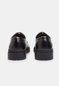 Scarpe in pelle nera con una superficie liscia, forma arrotondata e suole in gomma spesse; con bordi superiori di colore rosso in contrasto.