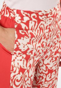 Czerwono-kremowe spodnie z wzorem na tkaninie, mające swobodny krój, z boczną kieszenią i elastycznym pasem dla wygody.