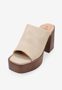 Sandalias de plataforma de ante beige con diseño de punta abierta, presentando un tacón grueso marrón y una textura suave.