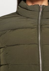 Olivengrøn dynejakke med høj krave, vandret quiltet tekstur og en sølvfarvet lynlås foran til lukning.