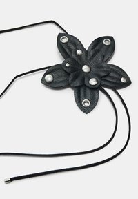 Svart läderblomma-formad berlock med silvernitar, med en texturerad yta och svarta snörband för justerbar längd.