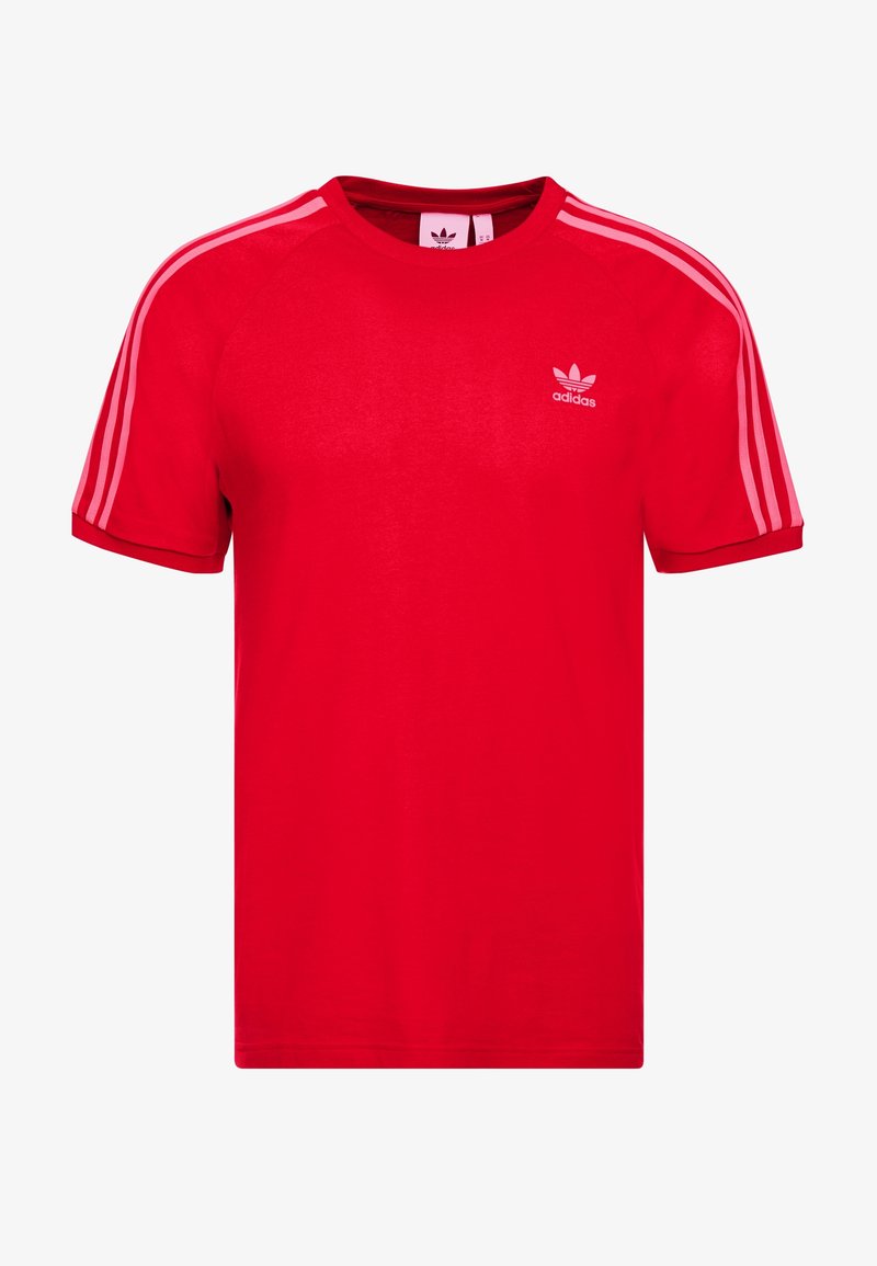 Červené bavlněné tričko s kulatým výstřihem, krátkými rukávy a třemi bílými pruhy na každém rameni. Obsahuje malé bílé logo adidas na hrudi.