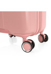 Maleta rígida rosa con patrón texturizado diagonal, que cuenta con cuatro ruedas negras con acentos plateados. Cierre de cremallera a lo largo del lado.