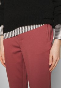 Roze op maat gemaakte broek met een gladde textuur, voorzien van een voorzak en een subtiele plooi, gecombineerd met een gestreepte, geribbelde zwarte trui eronder.