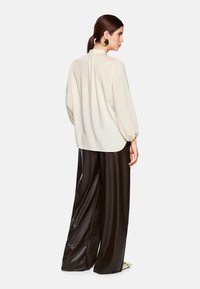 Cremfarbene Bluse mit langen Ärmeln und hohem Kragen, kombiniert mit schwarzen, weit geschnittenen, glänzenden Hosen. Glatte Textur; minimalistisches Design.