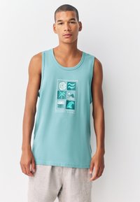 Bezroku turkīza krāsas tops ar grafiskiem viļņu, saules un palmu koku attēliem baltā krāsā. Izgatavots no kokvilnas, tas ir ērtā, vaļīgā stilā.