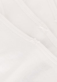Top in tessuto bianco con un delicato motivo a cuori, morbido al tatto, cuciture piatte e piccoli dettagli a fiocco sul collo.
