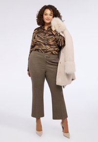 Blusa a righe zebrato marrone e nero, pantaloni corti a vita alta verde oliva, cappotto beige oversize con rifiniture in pelliccia e tacchi nudi.