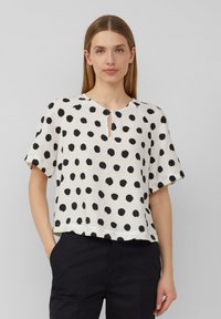 Haut à manches courtes, coupe ample en crème avec de grands pois noirs, présentant un décolleté en forme de trou de serrure et une surface légèrement texturée.