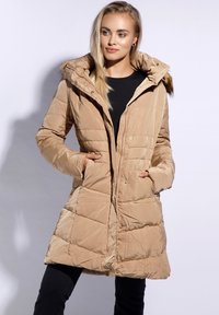 Beige péřová bunda s kapucí s kožešinovým lemem, prošívaný design, přední kapsy a zapínání na zip. Hladká textura a středně dlouhý střih.