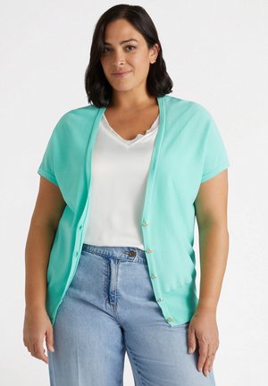 Mint green short-sleeve cardigan with a button front. Worn over a white top, paired with light blue high-waisted jeans. Smooth texture.