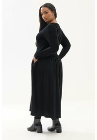 Mustassa pitkähihhaisessa mekossa on istuva bodice ja levenevä helma. Siinä on sivutaskut ja sileä kangas, joka on yhdistetty mustiin nilkkabootseihin.