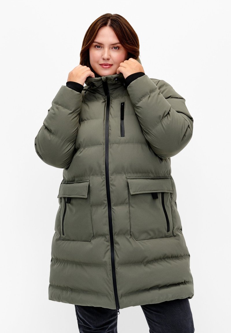 Manteau matelassé vert olive avec fermeture éclair et bouton-pression, comprenant deux poches avant et une poche poitrine zippée, en tissu texturé, avec une capuche.