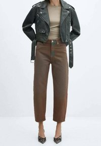 Žena v černé zkrácené kožené bundě, béžovém přiléhavém topu, hnědých širokých kalhotách s vysokým pasem a černých lodičkách s špičatou špičkou.