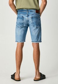 Pantalones cortos de mezclilla azul claro con un corte relajado, dobladillo enrollado y dos bolsillos traseros. Combinados con sandalias deslizables negras con suela de corcho.