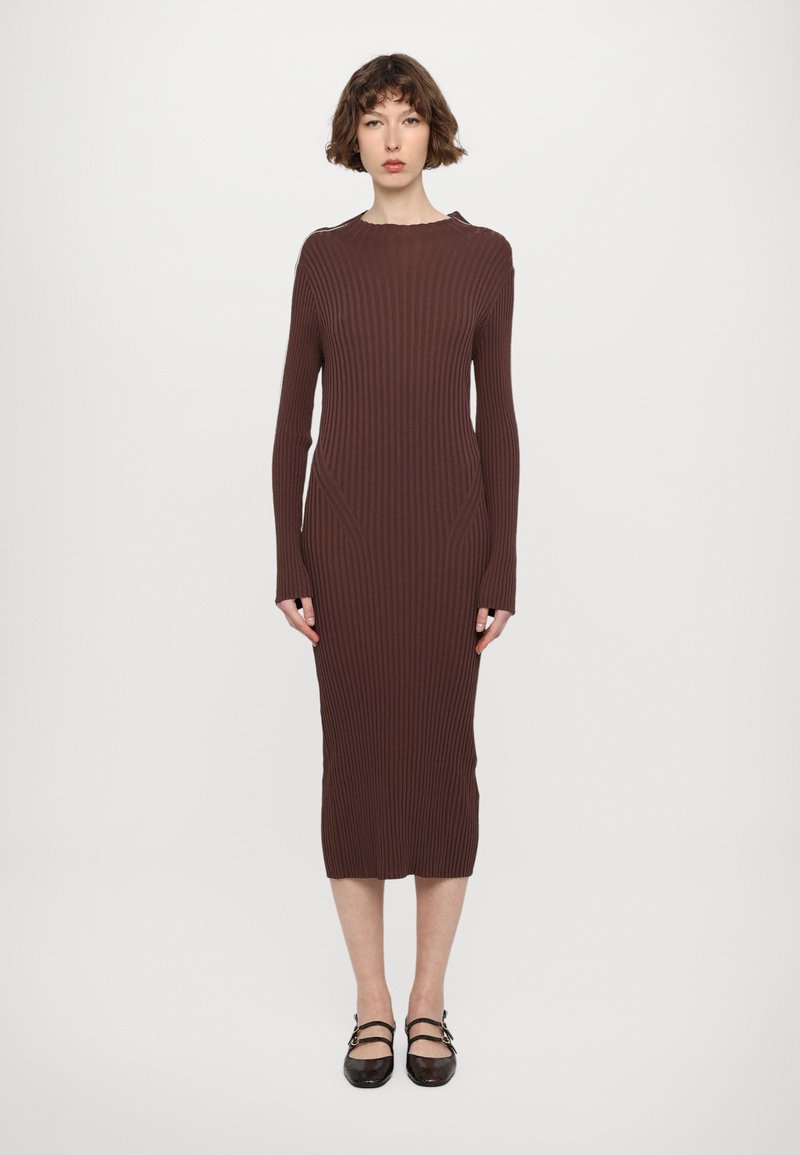 Rochie tricotată ribbed de culoare maro, cu mâneci lungi, decolteu în formă de cerc și siluetă ajustată, care se termină sub genunchi. Accentuată cu cusături laterale.
