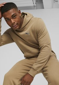 Felpa marrone e pantaloni jogger coordinati, realizzati in un morbido tessuto, con un logo Puma nero sul petto e accenti nei taschini laterali.