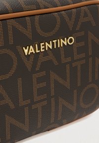 Brązowa torba z teksturowanej skóry, z wytłoczonym złotym logo „VALENTINO” i subtelnym wzorem z nazwą marki. Wykończona w kolorze koniakowym.