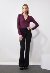 Dark purple ribbed long-sleeve top with a V-neck, paired with high-waisted black flared jeans and black platform shoes.