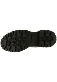 Suela de zapato de goma negra con profundas bandas de rodadura y un patrón texturizado para agarre. Diseño de tacón plano con una sección de mediasuela reforzada.