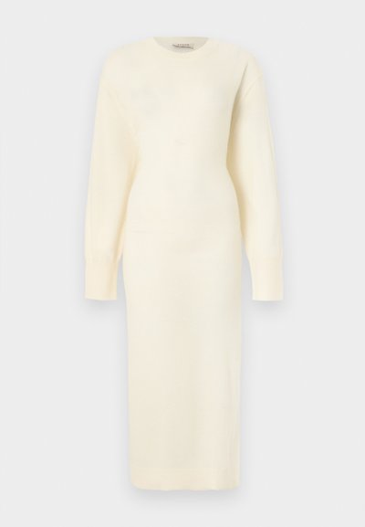 Κρεμ πλεκτό φόρεμα με μακριά μανίκια, λαιμόκοψη στρογγυλή και εφαρμοστή μέση, που φτάνει μέχρι το μέσο της γάμπας, παρουσιάζεται σε απλό φόντο.