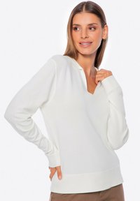 Biały dzianinowy sweter z dekoltem w serek, długimi rękawami i mankietami. Charakteryzuje się gładką fakturą i ściągaczem na dole. Minimalistyczny design.