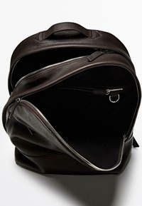 Brown leather backpack with a zippered opening, an interior zip pocket, and a top handle for carrying. Smooth texture, structured shape.