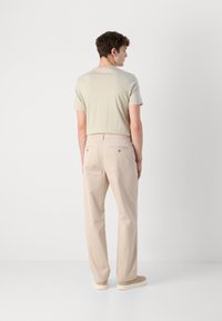 Beige bomullsbukser med rett ben-design, kombinert med en lys grønn kortermet t-skjorte. Uformell stil, minimalistiske detaljer.