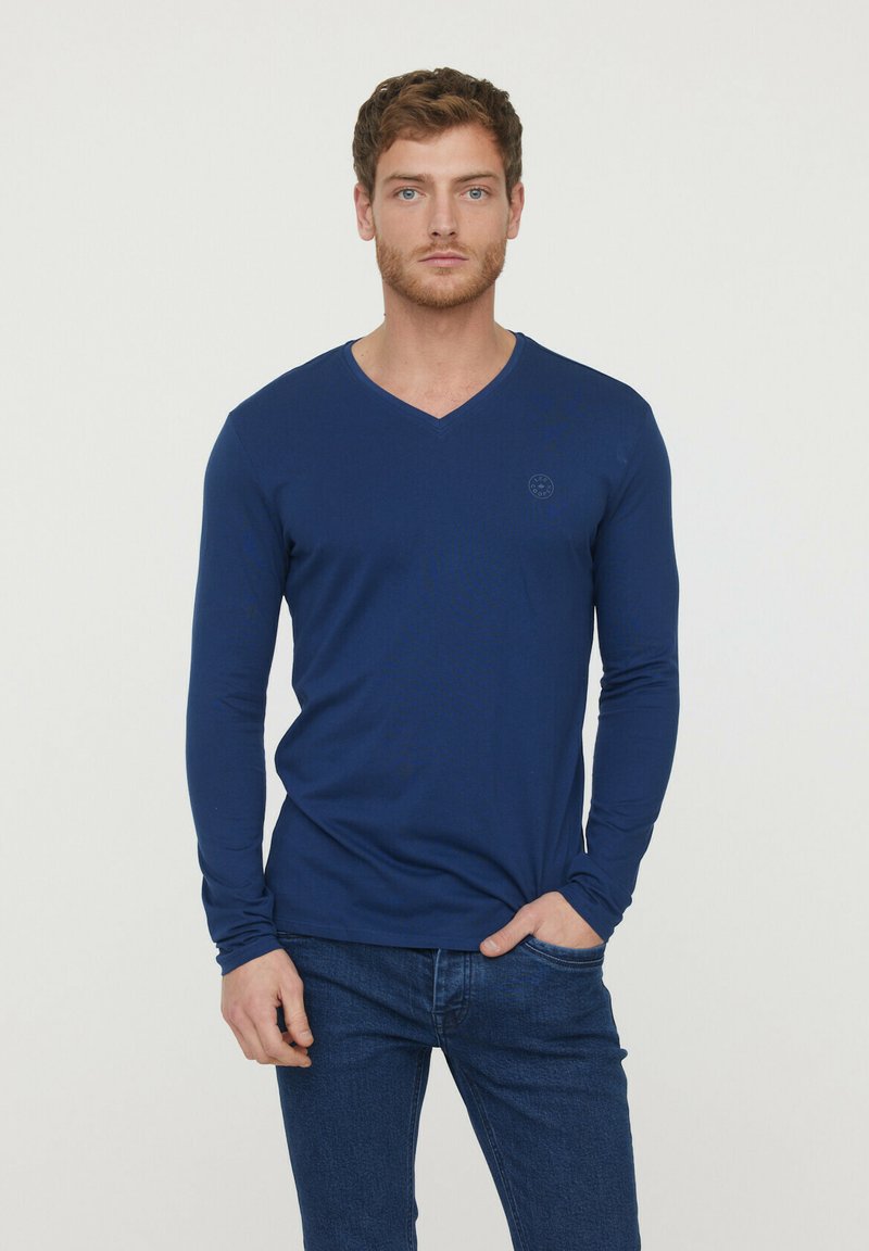 T-shirt à manches longues en V navy en coton doux, avec un logo discret sur la poitrine et une coupe ajustée.