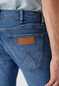 Blå denimjeans med en lädertagg från Wrangler, distinkt bakfickedesign med ett zickzackstitchmönster och en slim fit.