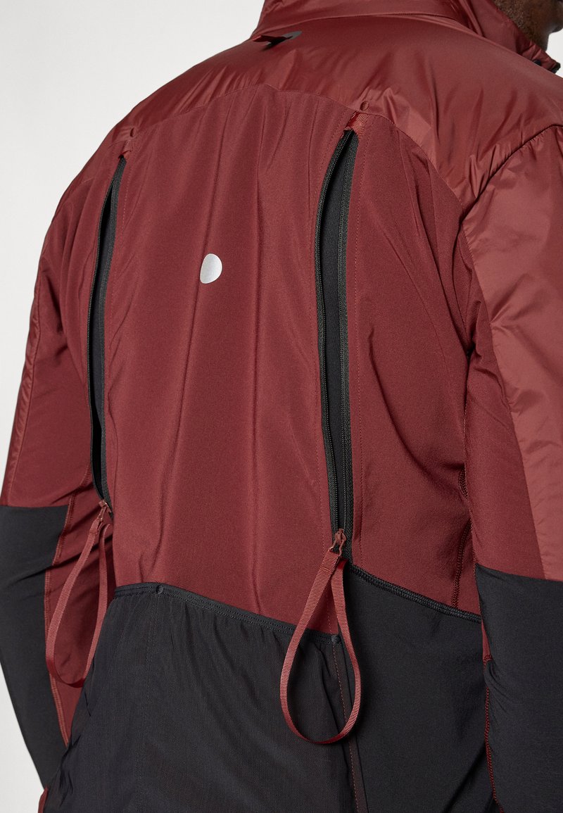 Veste bordeaux et noire avec des zips, matériaux texturés, et un point réfléchissant sur le haut du dos ; comprend des détails de resserrement et un design en panneaux.