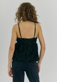 Camisola nera con motivo floreale realizzata in materiale testurizzato, dotata di spalline sottili e silhouette aderente, abbinata a pantaloni in denim scuro.