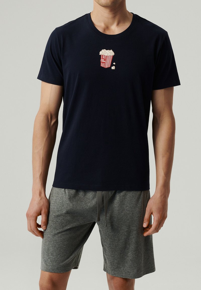 Granatowa bawełniana koszulka z nadrukiem graficznym popcornu w czerwono-białych kolorach, w połączeniu z szarymi szortami. Prosty okrągły dekolt i luźny krój.