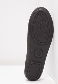 Semelle de chaussure en cuir noir avec bande de roulement texturée, logo circulaire de marque près du talon et talonnette nervurée, photographiée sur fond blanc.